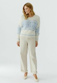 Gebreide trui in crème met lichtblauwe strepen, ronde hals en lange mouwen. Gecombineerd met beige opgerolde broek en beige hakken.