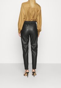 Brun satinblus med plisserad baksida, matchad med svarta faux läder taperade byxor och svarta högklackade skor, sedd bakifrån.