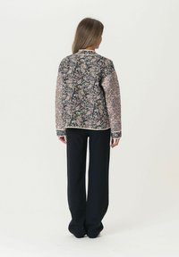 Bunda s květinovým vzorem a kontrastními rukávy, navy modrá základ a černé kalhoty. Texturovaná látka s podrobnými designovými prvky.