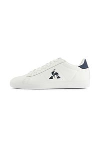 Sneaker bassa bianca con lacci bianchi, linguetta posteriore blu navy e un logo di gallo nero sul pannello laterale.