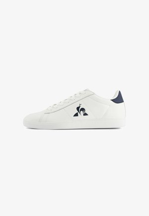 Baskets basses blanches avec des lacets blancs, un empiècement au talon bleu marine et un logo de coq noir sur le panneau latéral.
