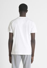 Camiseta blanca de manga corta hecha de algodón, con cuello redondo y corte recto. La vista posterior muestra un diseño minimalista y una textura suave.