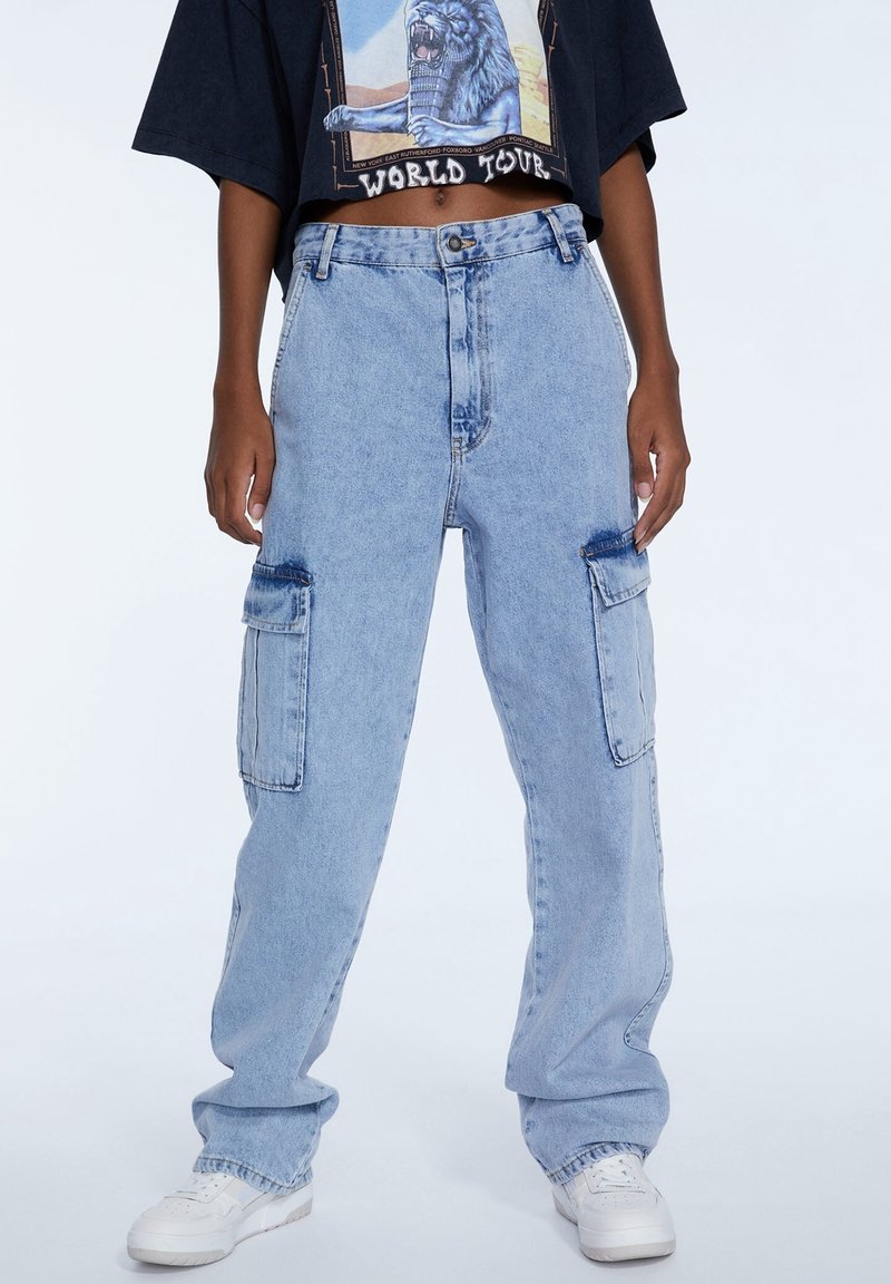 Pantalones cargo de mezclilla azul claro con un corte relajado, que cuentan con dos bolsillos laterales y costuras visibles. Combinados con una camiseta negra gráfica de corte crop.