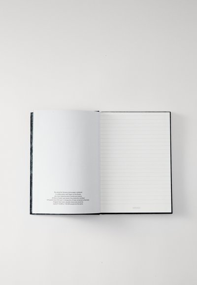 Quaderno in carta stone con copertina nera, aperto per mostrare l'interno a righe vuoto. Presenta una prima pagina grigia con testo stampato in basso.