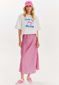 Bílá zkrácená tričko s grafikou "Pimp my Shrimp", růžová maxi sukně s puntíky a růžová kšiltovka, doplněno světle růžovými teniskami.