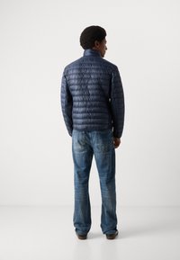 Marineblå polstret jakke med høy krage, med et quiltet mønster. Kombinert med lyseblå jeans, sett fra ryggen.