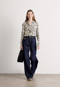 Long-sleeve, patterned blouse with ruffles, paired with wide-leg dark denim jeans. Black handbag and gray shoes complete the outfit.