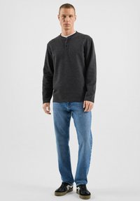 Szara koszula henley z długim rękawem na trzy guziki, zestawiona z jasnoniebieskimi dżinsami i czarnymi trampkami, charakteryzująca się gładką fakturą i luźnym krojem.