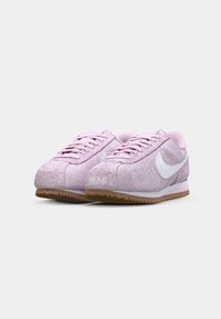 Light pink suede sneakers with white accents, rounded toe, and textured sole. Features lace-up design and cushioned collar for comfort.