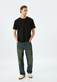 Zwart kortarm t-shirt met een borstzak, gecombineerd met jeans in een medium wash met een relaxte pasvorm en minimale vervaging. Witte sneakers.