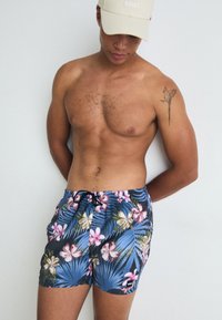 Costume de baie florale cu un fundal albastru, decorat cu flori hibiscus roz și albe și frunze de palmier. Talie elastică cu șnur negru, logo-ul mărcii.