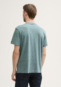 Camiseta verde jaspeada de manga corta, con un cuello redondo y un corte holgado. La tela presenta una textura sutil con acentos en azul oscuro.