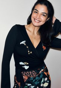 Melns garām piedurknēm krekls ar krāsainām izšūtiem zīmējumiem, tostarp zvaigznēm, roku un sirdi, kombinēts ar rakstainu daudzkrāsu svārku.