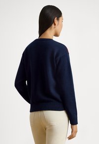 Μπλε ναυτικό πλεκτό πουλόβερ με στρογγυλή λαιμόκοψη, ριμπ μανσέτες και τελείωμα. Διαθέτει ξεχωριστή αντίθετη λεπτομέρεια στο ώμο.