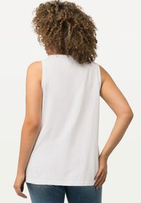 Witte mouwloze top met een gladde textuur, ronde halslijn en een relaxte pasvorm, gecombineerd met blauwe denim jeans.