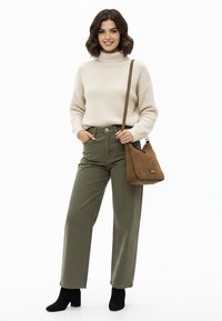 Femme portant un pull à col roulé beige, un pantalon taille haute vert olive, des bottines noires et un sac à bandoulière marron.