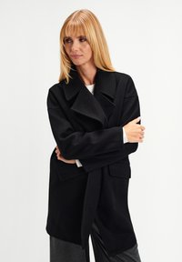Black wool coat with a notched collar, long sleeves, and front pockets. Features a loose fit and a tie belt at the waist.