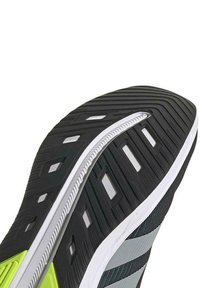Zapatilla deportiva negra con una suela de goma texturizada, detalles en blanco y verde, y un diseño aerodinámico que incluye rayas grises reflectantes.