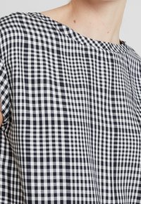 Černobílý top s kostkovaným vzorem, kulatým výstřihem, krátkými rukávy a mírně strukturovanou bavlněnou tkaninou.