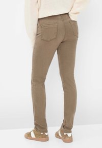 Slim-fit, olijfgroene broek met een zachte, gestructureerde afwerking, voorzien van achterzakken en een middellange tailleband, gecombineerd met tan sneakers.