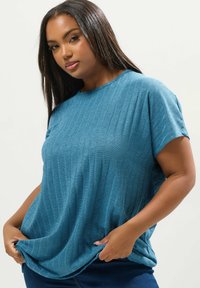 Sininen ribbineulepaita, jossa on lyhyet hihat ja pyöreä kaula-aukko. Paita on rento ja siinä on hienovarainen tekstuuri, jota pidetään helman kohdalta käsillä.