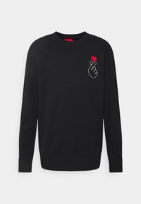 Sudadera negra de tejido suave con mangas largas, cuello redondo y un gráfico de una mano con un detalle de corazón rojo en el pecho.