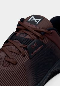 Κοντινό πλάνο σε καφέ και μαύρο αθλητικό παπούτσι με υφασμάτινη υφή, καφέ κορδόνια και διακριτικό λογότυπο στη γλώσσα και στην πλευρική επιφάνεια.