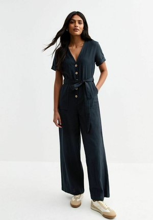 Giubbotto blu navy con maniche corte, scollatura a V, bottoni in legno, cintura da annodare e due tasche sul davanti, realizzato in un tessuto leggero.
