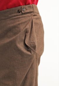 Hnědé kalhoty vyrobené z texturované látky s jemným tečkovaným vzorem. Disponují zapínáním na knoflík a bočními sklady pro dekorativní detail.