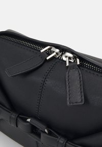 Clutch in pelle nera con finitura testurizzata, dotata di chiusura a zip in argento, dettagli cuciti e un accento decorativo a fiocco.