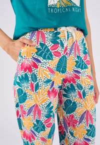 Pantaloni colorati e con motivi presentano grandi disegni floreali e fogliari in turchese, rosa, giallo e viola su sfondo bianco, con vita regolabile con cordoncino.