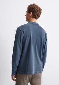 Langsleeve blauwe polo met een zachte stof en een relaxte pasvorm, voorzien van een kraag en een rechte zoom, gedragen met beige broek.