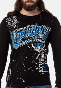 Schwarzes Langarm-T-Shirt mit weißen und blauen Grafikdrucken, das Spritzdetails und Texte wie "Legendär" und "Speedway 1996" zeigt.