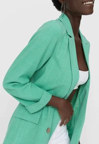 Groene linnen blazer met een sjawlkragen, lange mouwen en een enkele knoopsluiting. Heeft een voorkantzak en een relaxte pasvorm.