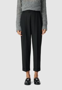 Zwarte op maat gemaakte broeken met een ontspannen pasvorm, voorzien van een omslagzoom en een gladde textuur, gecombineerd met een fluffy grijs trui en glanzende zwarte schoenen.