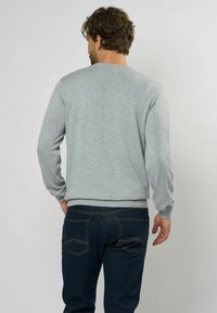 Grijze sweatshirt van zacht materiaal, met een ronde hals, lange mouwen, geribde boorden en een zoom, gedragen met donkerblauwe jeans.