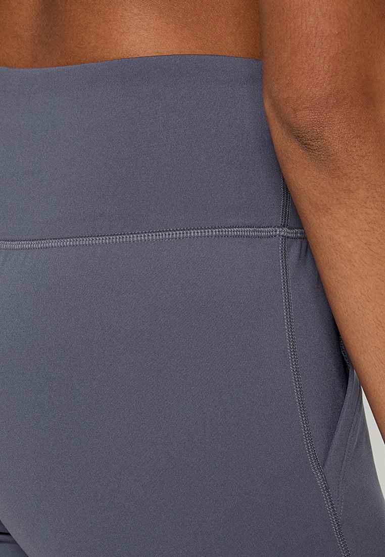 Leggings gris extensibles avec une large taille, une texture lisse et des détails de couture subtils. Aucune poche n'est visible dans cette vue.