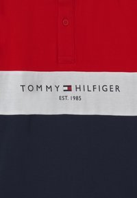 Polo tričko s červenými, bílými a námořnickými vodorovnými pruhy, zapínacím límcem a logem "TOMMY HILFIGER EST. 1985" na přední straně.