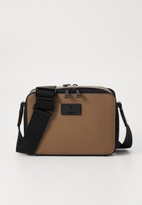 Rjava teksturirana torbica čez ramo s črnim nastavljivim trakom, dvojnim zadržnim zapiranjem in majhno črno logotipno nalepko na sprednji strani.