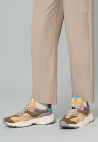 Sneaker multicolori con un mix di accenti marroni, gialli, verdi e rosa. Presentano una suola spessa, materiali testurizzati e sovrapposizioni con motivi.