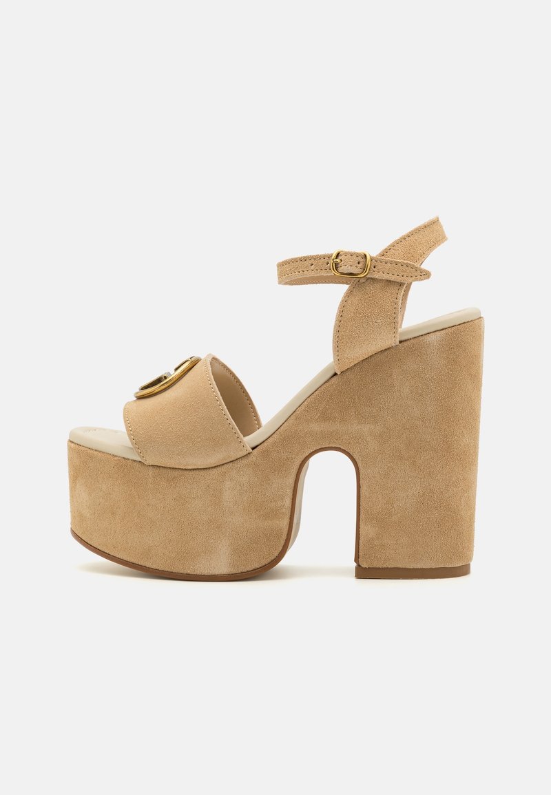 Sandales compensées à talons hauts en daim beige, avec un bout arrondi, une bride à la cheville et un accent circulaire doré à l'avant, surface texturée.