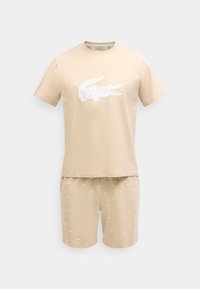 Μπεζ κοντομάνικο μπλουζάκι με μεγάλο λευκό λογότυπο κροκοδείλου και αντίστοιχες σορτς με μικρά λευκά σχέδια κροκοδείλων.