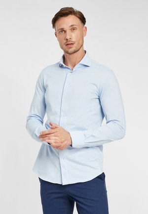 Himmelblaues Hemd mit Knöpfen, leicht glänzend, lange Ärmel und abgerundetem Saum. Der Stoff wirkt weich mit einer glatten Textur.