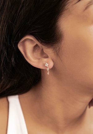 Goldfarbene Ohrringe mit mehreren funkelnden Kristallen, die ein blumiges Design und einen herabfallenden Stil aufweisen, sichtbar vor einem neutralen Hintergrund.