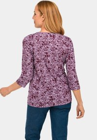Paars bloemenpatroon shirt met driekwart mouwen, zachte stof, ronde halslijn en een rechte zoom, gecombineerd met donkerblauwe jeans.
