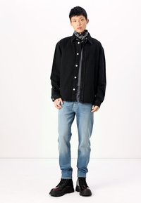 Camisa de mezclilla negra con botones plateados, superpuesta sobre una camiseta gris; jeans azul claro; botas negras con cordones y suelas gruesas; bufanda estampada.