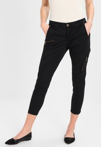 Svarta korta byxor med smal passform, med sidofickor med dragkedja, guldfärgad hårdvara och en mjuk tygtextur.