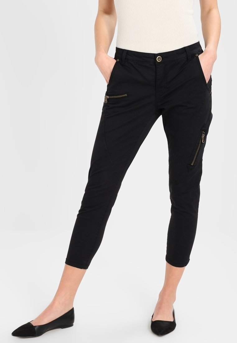 Svarta korta byxor med smal passform, med sidofickor med dragkedja, guldfärgad hårdvara och en mjuk tygtextur.