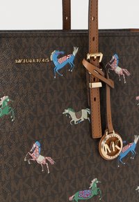 Καφέ τσάντα tote Michael Kors με επαναλαμβανόμενο λογότυπο MK, πολύχρωμες απεικονίσεις αλόγων, δερμάτινα λουριά και χρυσό στρογγυλό έμβλημα MK.