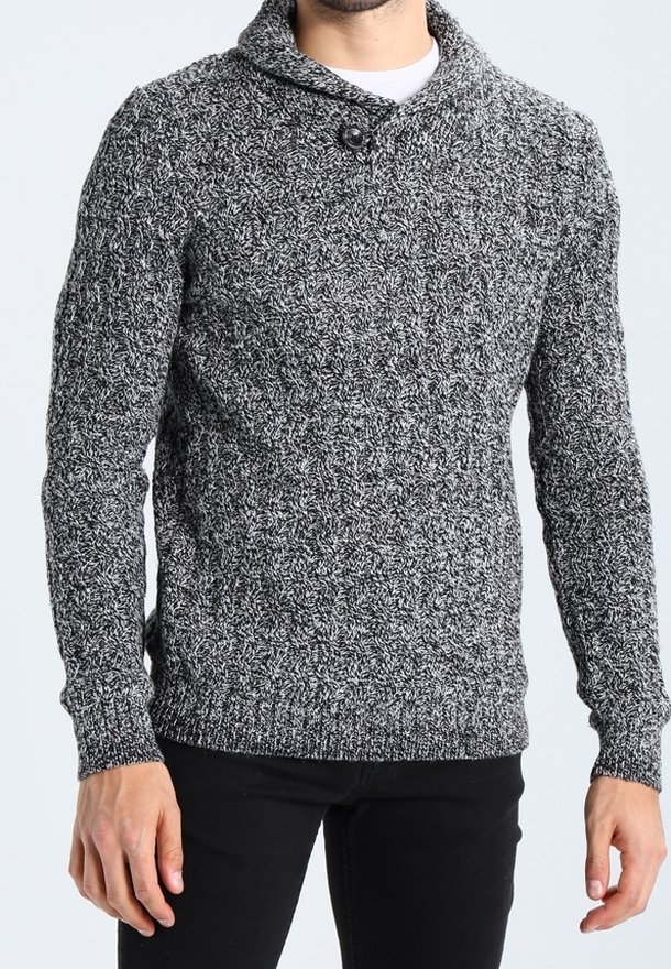 Homme portant un pull en maille texturée gris et noir avec un col châle et un seul bouton, associé à un pantalon noir.